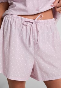 Lichtroze slaapshorts met een tailleband met trekkoord, voorzien van een subtiel wit stippenpatroon en een relaxte pasvorm. Zacht, ademend materiaal.