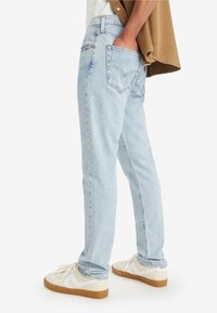 Light blue denim jeans with a relaxed fit, featuring a stitched back pocket design and a high waist. Paired with white sneakers.