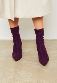 Botas de tobillo de ante moradas con un diseño arrugado, puntera afilada y detalle de cremallera lateral. Presenta costuras en contraste a lo largo de las costuras.