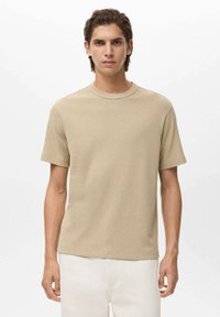 Tricou bej cu mânecă scurtă, confecționat dintr-un material texturat, cu gât rotund, asortat cu pantaloni de culoare deschisă. Fără modele sau elemente metalice vizibile.