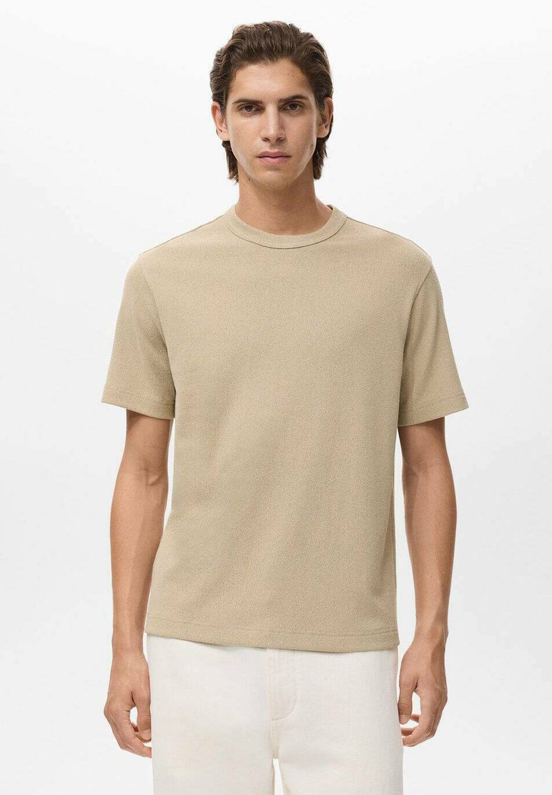 Tricou bej cu mânecă scurtă, confecționat dintr-un material texturat, cu gât rotund, asortat cu pantaloni de culoare deschisă. Fără modele sau elemente metalice vizibile.