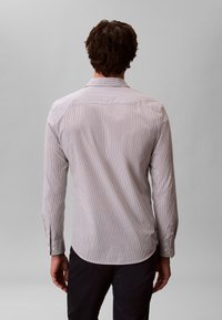 Chemise à manches longues gris clair avec fines rayures verticales, poignets boutonnés et ourlet incurvé. Col uni avec une texture lisse.