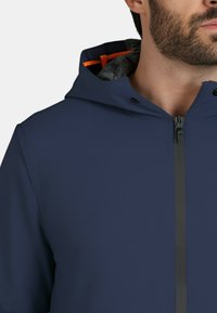 Marineblå hættejakke med en glat tekstur, frontlynlås og kontrasterende orange detaljer på det indre foer.