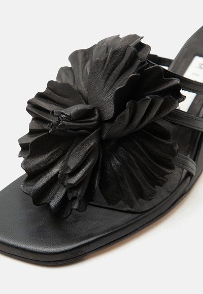 Μαύρο σανδάλι με μεγάλο υφασμάτινο λουλούδι από δέρμα σε τετράγωνη μύτη και λεπτές λουρίδες.