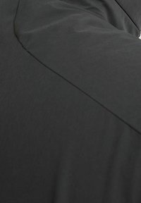 Primo piano di un tessuto nero, che mostra una consistenza liscia con un leggero brillantezza. Presenta cuciture asimmetriche e un design dal taglio rilassato.