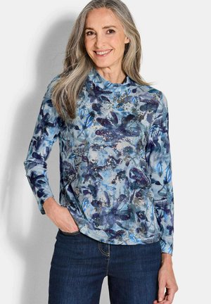 Langärmliges Hemd in verschiedenen Blautönen mit floralem Muster. Glattes, leichtes Gewebe. Rundhalsausschnitt. Kombiniert mit dunklen Jeans.