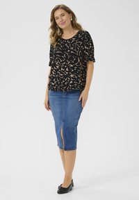 T-shirt noir à manches courtes avec un motif abstrait beige, associé à une jupe en denim arrivant au genou avec une fente sur le devant. Portée avec des ballerines noires.