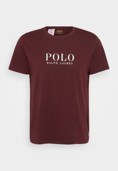Burgundska bombažna majica s krojnim ovratnikom, ki prikazuje belo besedilo "POLO" in "RALPH LAUREN". Podrobnost s stransko oznako pri robu.