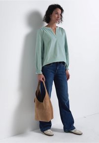 Blouse vert clair à manches longues avec un décolleté en V et des poignets froncés, associée à un jean bleu foncé et un sac à épaule en suède beige.
