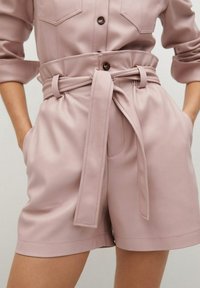 Jasnoróżowe szorty wykonane z gładkiego materiału, z paskiem w talii, bocznymi kieszeniami oraz przeszyciami wzdłuż dołu i kieszeni.