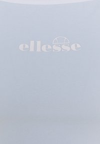 Top ajustado de color azul claro fabricado en tejido acanalado. Presenta un logotipo blanco de "ellesse" centrado en la parte delantera. Textura suave, sin patrones.