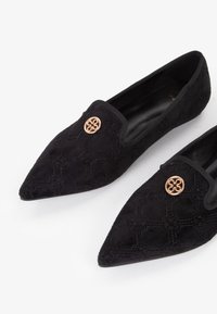 Ballerine in suede nero con punta affusolata, caratterizzate da motivi testurizzati, bordo elastico e un prominente bottone decorativo in tonalità oro.
