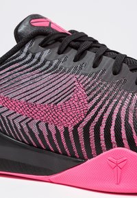 Urheilukengät, joissa on musta ja vaaleanpunainen muotoilu, teksturoitu kangas ja kalastajaläikkiä pohjassa. Silmiinpistävät vaaleanpunaiset korostukset korostavat brändäystä.