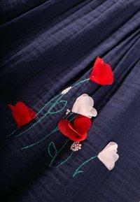 La tela azul marino presenta flores bordadas en rojo y blanco, con tallos y hojas verdes. La superficie texturizada realza el detalle visual.
