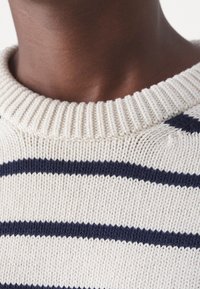 Pull en maille crème avec des rayures horizontales bleu foncé et un col côtelé. La texture est lisse avec un poids moyen.