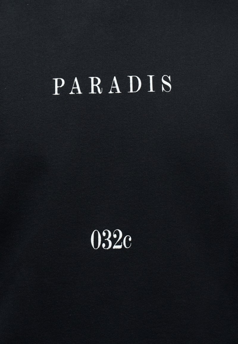 Tissu noir avec le texte blanc "PARADIS" centré près du haut et "032c" centré en dessous en plus petit format.