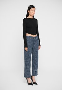 Black fitted long-sleeve top paired with loose blue textured pants featuring a speckled pattern, complemented by black high-heeled shoes.