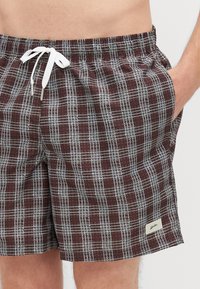 Σορτς κολύμβησης με καρό σχέδιο σε σκούρο κόκκινο και γκρι χρώμα, με ζωνάκι που ρυθμίζεται, πλαϊνές τσέπες και μια μικρή ετικέτα λογότυπου στο κάτω στρίφωμα.