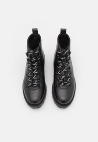 Botas de senderismo de cuero negro con una superficie texturizada, con cordones grises y blancos, de altura hasta el tobillo y una suela de goma resistente.