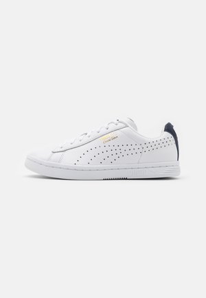 Baskets basses blanches avec panneaux latéraux perforés, texte doré "Puma Court Star" et languette de talon noire, présentées de profil sur fond blanc.