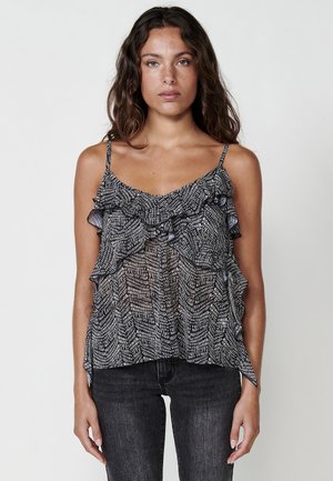 Camisole à motifs noir et blanc avec des accents volantés, des bretelles spaghetti fines et un tissu doux semi-transparent. Associé à un jean noir.