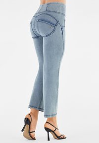Jean taille haute bleu clair avec un design unique de poche arrière, coupe slim et ourlet effiloché, associés à des sandales à talons hauts noires.