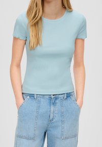 Top corto a maniche corte blu chiaro a costine con scollo rotondo e dettagli orlo sfilacciato, abbinato a jeans in denim chiaro a vita alta.