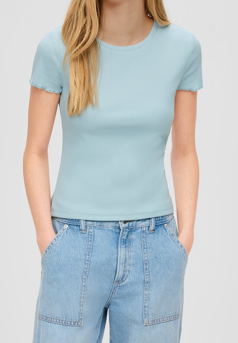 Top corto a maniche corte blu chiaro a costine con scollo rotondo e dettagli orlo sfilacciato, abbinato a jeans in denim chiaro a vita alta.