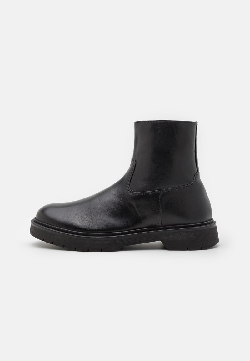 Botas de tornozelo em pele preta com uma textura suave, biqueira arredondada e painéis laterais elásticos; sola de borracha robusta para maior durabilidade.