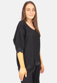 Schwarze, locker sitzende Bluse mit V-Ausschnitt, kurzen Ärmeln und strukturiertem Stoff. Verfügt über einen glatten Saum und dezenten Glanz an den Kanten.