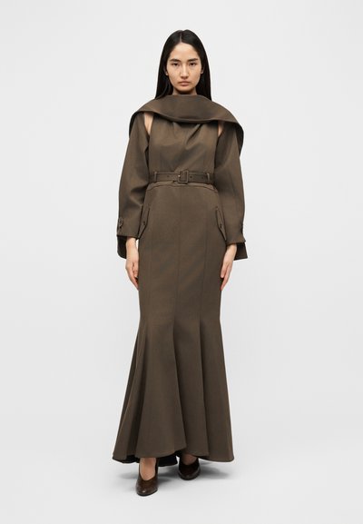 Longue robe marron avec un corsage ajusté et une jupe évasée, dotée d'un col drapé unique et d'une taille ceinturée. Le tissu présente une texture lisse.