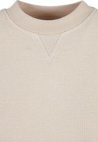 Vêtement en maille couleur crème avec une texture côtelée, présentant un large décolleté et un accent en forme de V à l'avant.