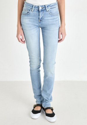 Light blue denim jeans with a slim fit, mid-rise waist, subtle fading, and traditional five-pocket design, paired with black and white shoes.