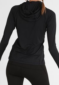 Zwarte sportieve lange mouw top met een capuchon, met een gladde textuur, aansluitend ontwerp en platte stiksels voor comfort en bewegingsvrijheid.