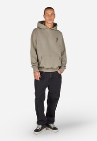 Hettegenser i dempet beige, med frontlomme og ribbestrikkede mansjetter. Sammen med svarte, løse jeans og joggesko med grå base og mørke detaljer.