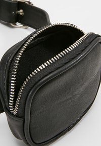 Pochette en cuir noir de forme arrondie, dotée d'une fermeture éclair argentée et d'une texture lisse. L'intérieur est doublé de tissu noir.