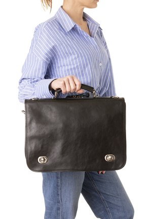 Attaccatura in pelle nera con un design elegante, caratterizzata da dettagli in metallo argentato e una maniglia superiori, tenuta da una persona che indossa una camicia a righe.