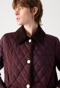 Gequilted jas in diep bordeaux met een corduroy kraag. Voorzien van gouden knopen en contrasterende stoftexturen. Tailored fit.