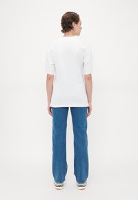 Vit bomulls t-shirt med korta ärmar, rak passform och rundad halsringning, ihop med avslappnade blå denimbyxor och ljusa sneakers.