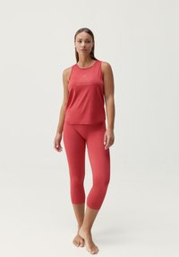 Czerwony sportowy top na ramiączkach z białym drukowanym tekstem, w połączeniu z dopasowanymi leginsami do kostek. Oba elementy wykonane są z gładkiego, elastycznego materiału.