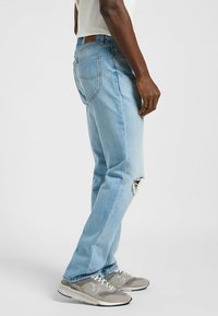 Jeans in denim blu chiaro con una vestibilità rilassata, caratterizzati da un ginocchio strappato, cinque tasche e un'etichetta in pelle marrone in vita.