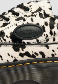 Κοντινό πλάνο μαύρου και λευκού παπουτσιού Dr. Martens με βούλες, μαύρια κορδόνια, μαύρη σόλα και κίτρινες ραφές.