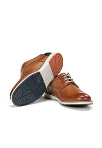 Zapatos de cuero marrón claro con un acabado liso, diseño con cordones, suela de goma en contraste azul marino y roja, y patrones de agarre texturizados en la suela exterior.