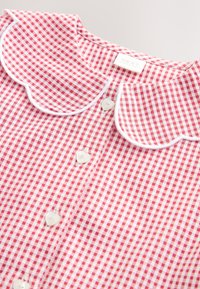 Chemise à carreaux rouges et blancs avec col festonné bordé de blanc et boutons blancs en forme de cœur sur le devant.