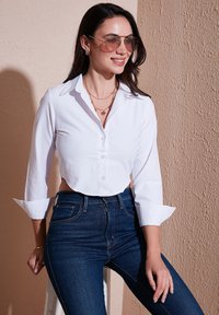Witte cropped blouse met knopen, lange mouwen en opgerolde manchetten, gecombineerd met donkerblauwe hooggewaist jeans. Glad materiaal met een kraagdetail.