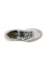 Zapatilla deportiva de color gris claro con parte superior de malla y ante, con acentos en gris oscuro, cordones planos y suela de goma blanca con un detalle en amarillo neón.