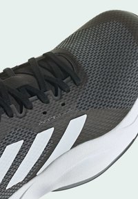 Zwarte en grijze sportschoen met een gestructureerd bovenstuk, zwarte veters en witte strepen aan de zijkant. Heeft een gevoerde witte zool.