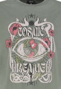 Grünes Baumwoll-T-Shirt mit einem grafischen Design, das ein Auge, florale Motive und den Text "COSMIC DREAMER" zeigt, akzentuiert mit schwarzen und pinken Details.