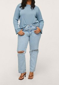 Jasnoniebieski dzianinowy top z długim rękawem w połączeniu z jasnoniebieskimi, prostymi dżinsami z przetarciami na kolanach oraz brązowymi sandałami na paski.