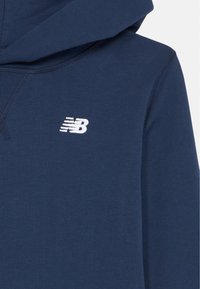 Hoodie azul marinho feito de tecido macio, com um bolso tipo canguru, punhos canelados e um logótipo da New Balance em branco no peito.